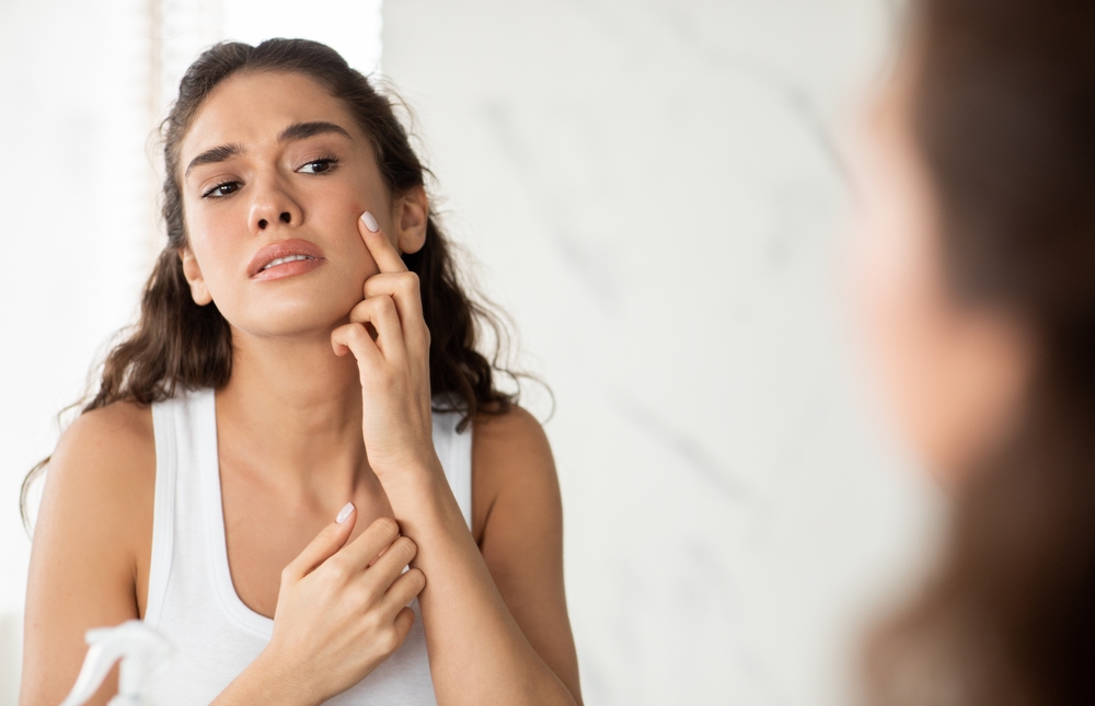 Stock photograph of a model: a woman with tousled hair touches her cheek and looks at herself in a mirror